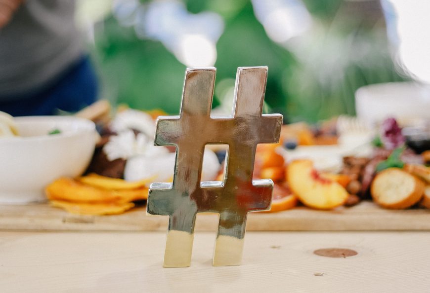 A metallic hashtag with a plate of fruit in the background.