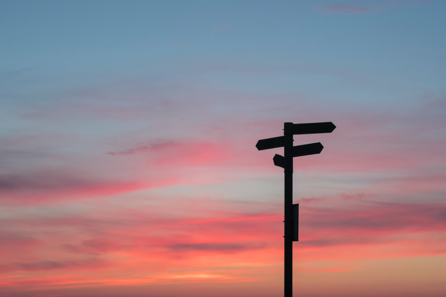 A signpost that points several different directions with a sunset in the background.