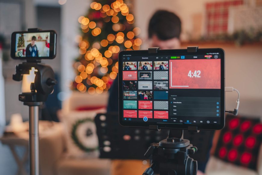 A smartphone and a tablet set up on tripods recording someone with a Christmas-themed background