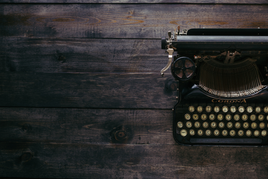 A black typewriter sitting on a dark wooden background, seen from an aerial view.